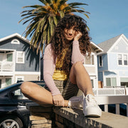 Women's Monterey Sneaker in Bleach canvas, worn with shorts by a person seated on a seawall