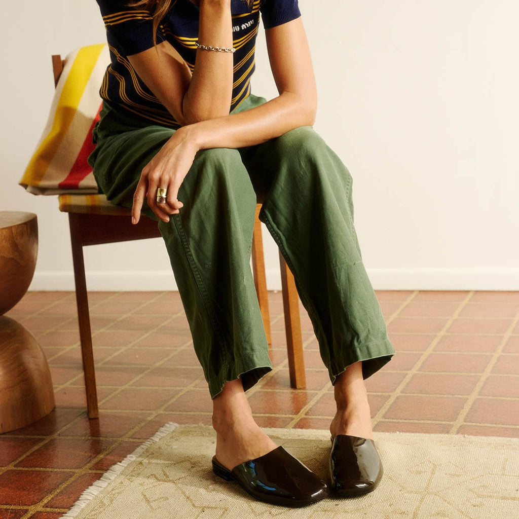 Women's Sadie Slide in Dark Chocolate rubber, worn by a person seated in a chair in olive pants