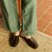 Women's Sadie Slide in Dark Chocolate rubber, worn with olive pants on a terracotta tile floor