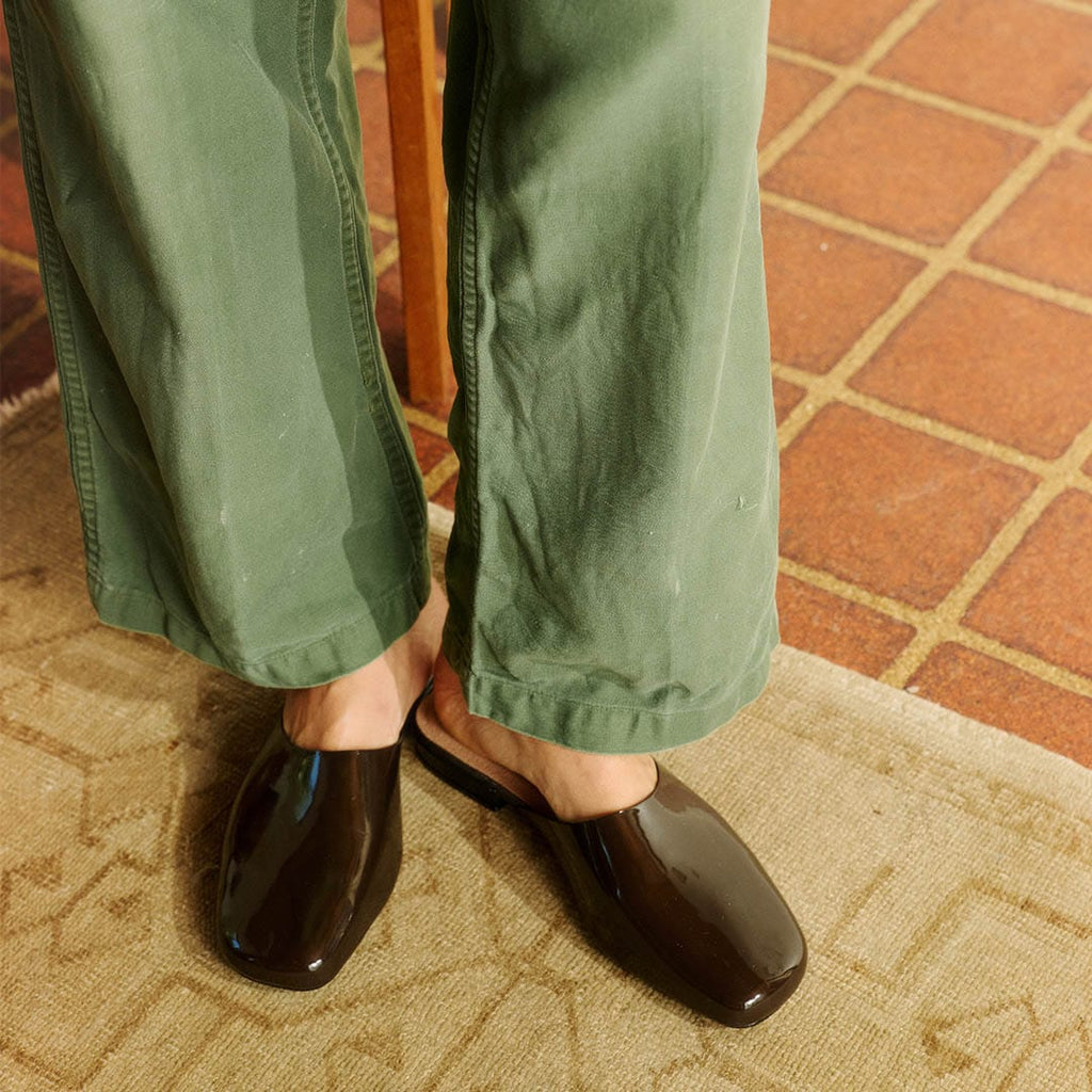 Women's Sadie Slide in Dark Chocolate rubber, worn with olive pants on a terracotta tile floor