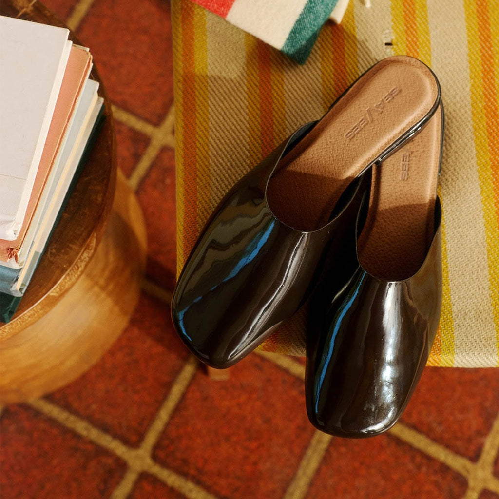 Women's Sadie Slide in Dark Chocolate rubber, pair resting on a terracotta tile floor with books