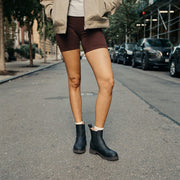 Women's Salt Creek Boot in Black leather, worn with biker shorts, standing on a city street
