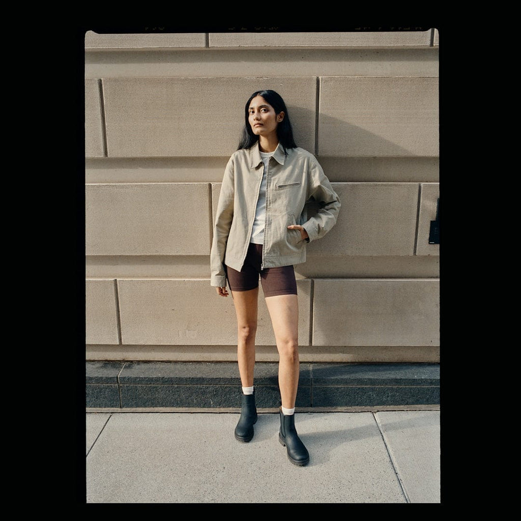Women's Salt Creek Boot in Black leather, worn by a person standing against a stone wall in a tan jacket
