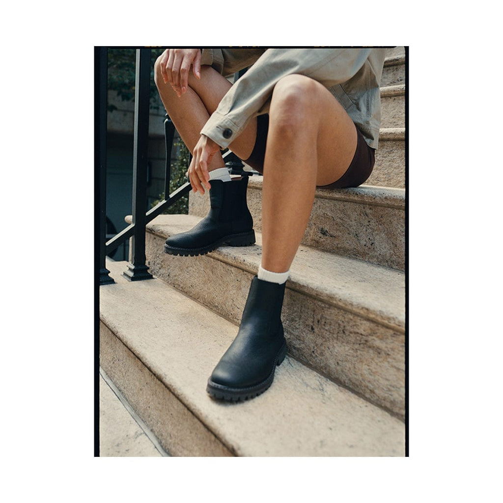 Women's Salt Creek Boot in Black leather, worn by a person seated on stone steps with bare legs