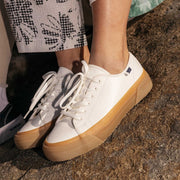 Women's SeaChange LTT sneaker in White/Gum corn leather, close-up worn with printed pants and bare ankles, gum sole visible