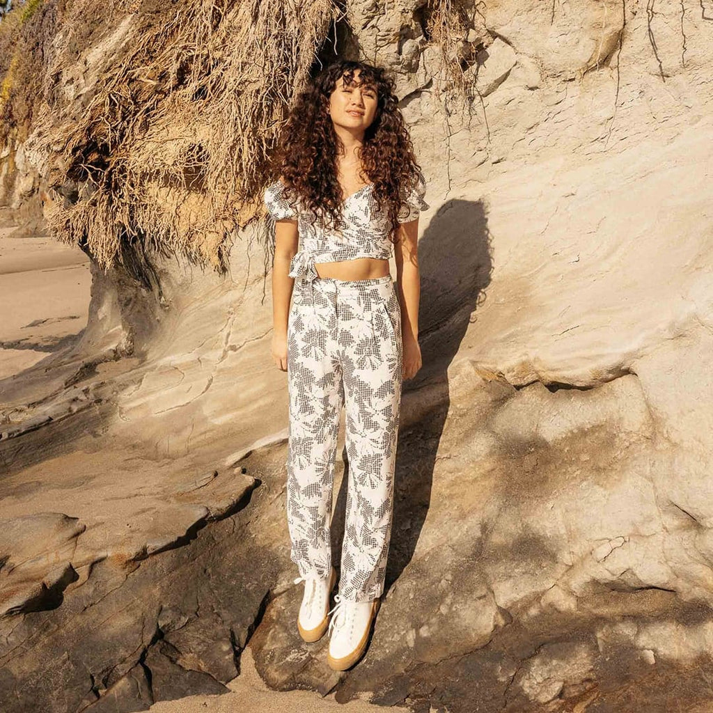 Women's SeaChange LTT sneaker in White/Gum corn leather, worn with printed pants by a person standing among sandstone rocks