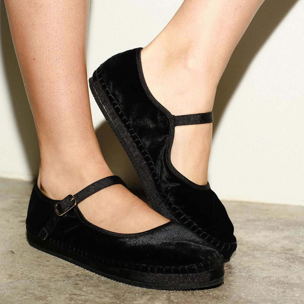 Women's Carlyle Mary Jane in Black velvet, worn with a strap closure on a concrete floor, close up