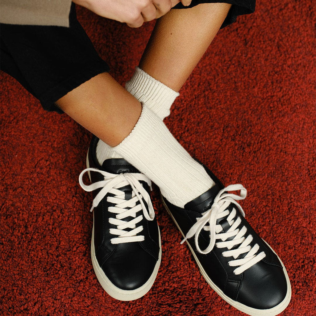 Women's Diamond Cup sneaker in Black leather, worn with white socks, pair seated on a red rug