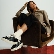 Women's Diamond Cup sneaker in Black leather, worn by a woman seated in a brown armchair