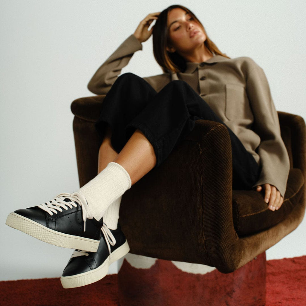 Women's Diamond Cup sneaker in Black leather, worn by a woman seated in a brown armchair