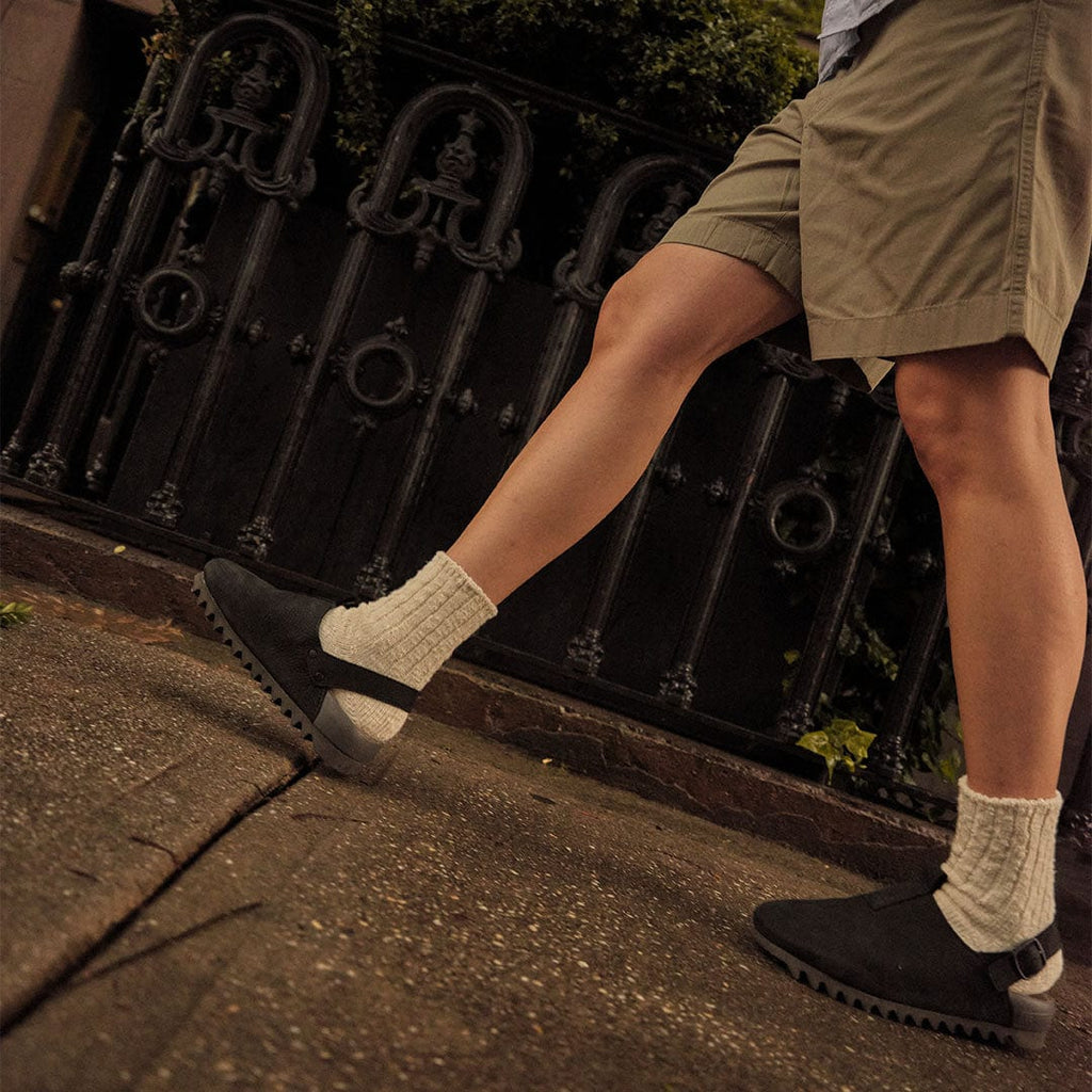 Women's Tahoe Trekker sandal in Black leather, worn with khaki shorts and beige socks, walking on a sidewalk