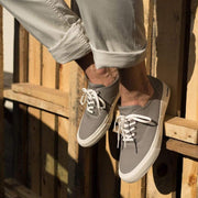 Men's Legend Sneaker in Granite Grey canvas, close-up with laces, feet propped on wooden slats