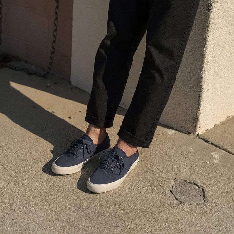 Men's Legend Sneaker in True Navy canvas, worn with dark cropped pants on pavement