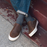 Men's Hawthorne Slip On in Elmwood leather, close-up worn with cuffed jeans and gray socks on a painted porch