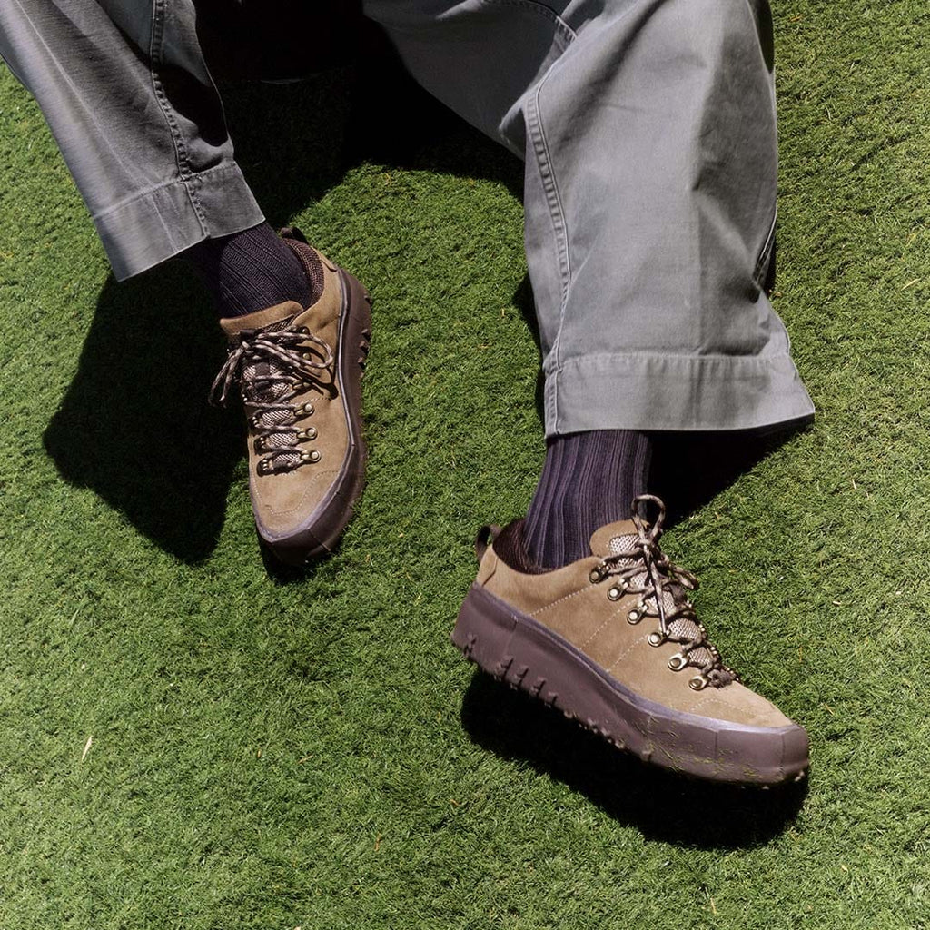 Men's Ridge Urban Hiker hiking sneaker in Desert Palm suede, worn with gray pants and dark socks on green grass