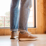 Men's Acorn Trainer sneaker in Tan suede, close-up worn with jeans in front of a window
