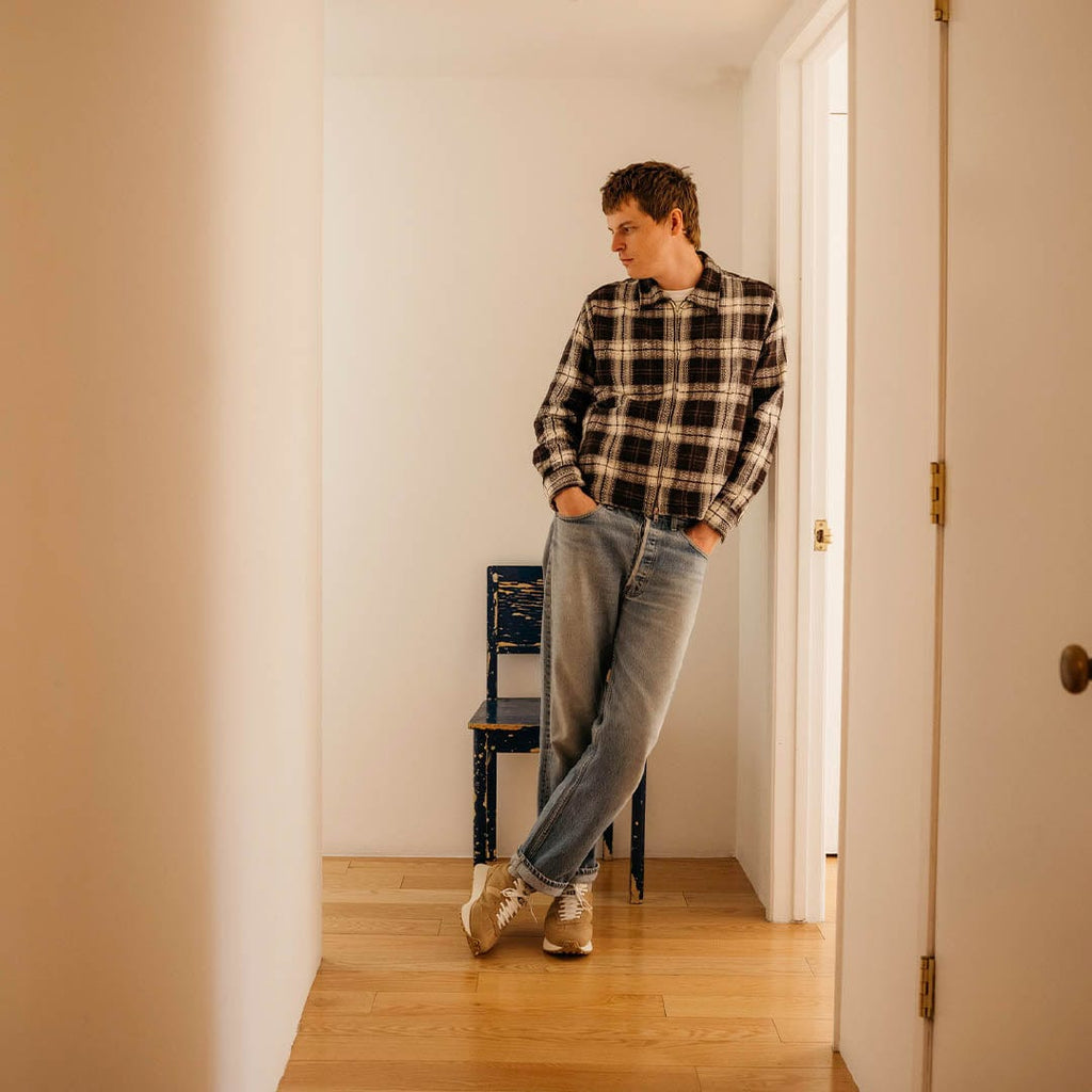 Men's Acorn Trainer sneaker in Tan suede, worn with jeans by a person leaning in a doorway