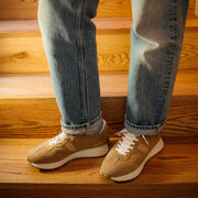 Men's Acorn Trainer sneaker in Tan suede, close-up worn with jeans on wooden stairs