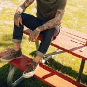 Men's Maslon Desert Boot in Elmwood leather, worn with cuffed jeans by a person seated on a red picnic table