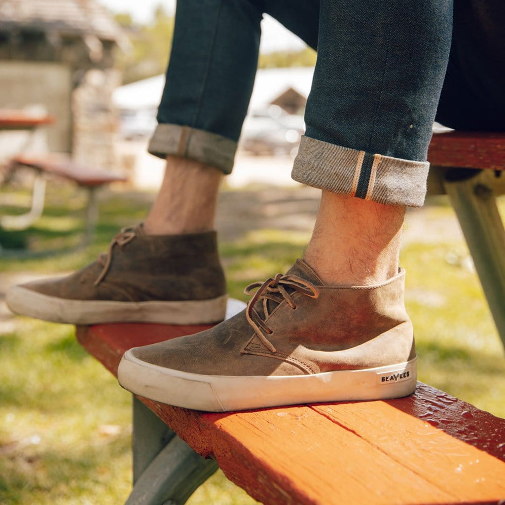 Men's Maslon Desert Boot in Elmwood leather, front close-up worn with cuffed jeans on a red bench