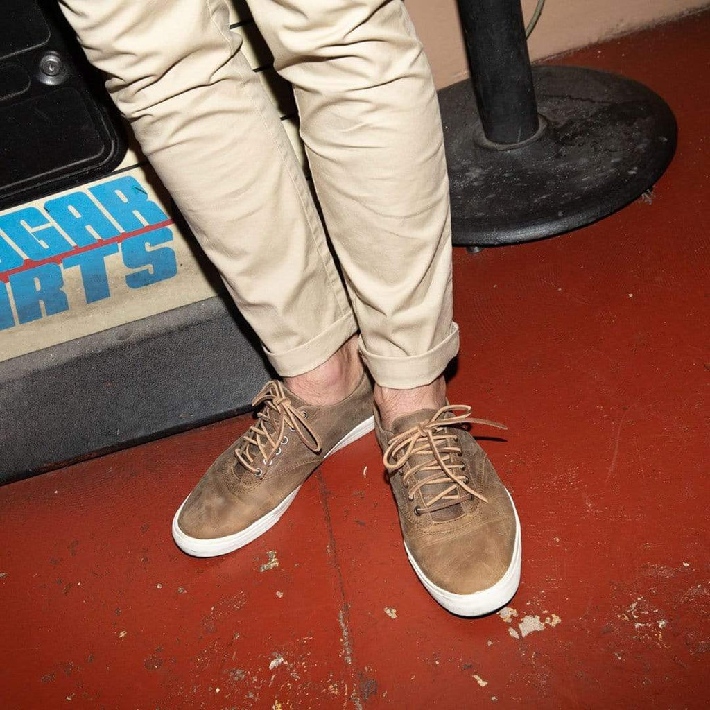 Men's Hermosa Sneaker in Elmwood leather, close-up worn with khaki pants on a red floor