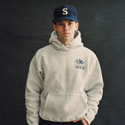Person in an oatmeal SeaVees x Camber hoodie and navy ballcap, front view