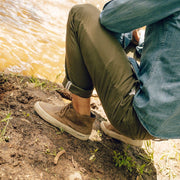 Men's Maslon Desert Boot in Elmwood leather, worn with olive pants by a person seated on grass