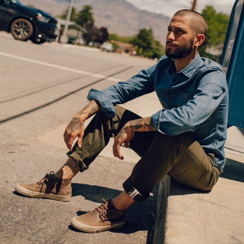 Men's Maslon Desert Boot in Elmwood leather, worn with olive pants by a person seated on a curb