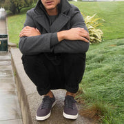 Men's Hermosa Sneaker in Slate Navy canvas, worn by a person crouching on a grassy ledge in a gray jacket