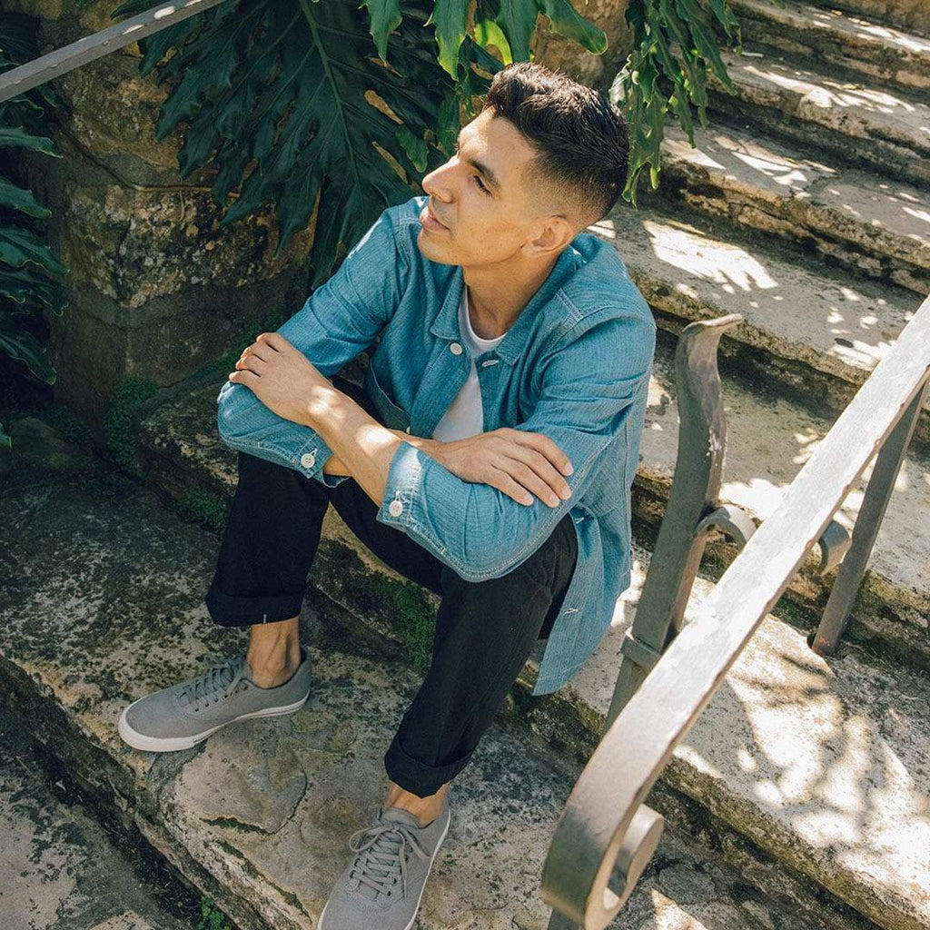 Men's Hermosa Sneaker in Tin Grey canvas, worn with dark pants by a person seated on outdoor stairs