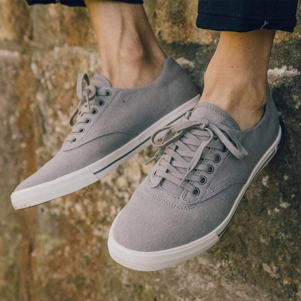 Men's Hermosa Sneaker in Tin Grey canvas, close-up of both shoes with laces, worn on a stone wall