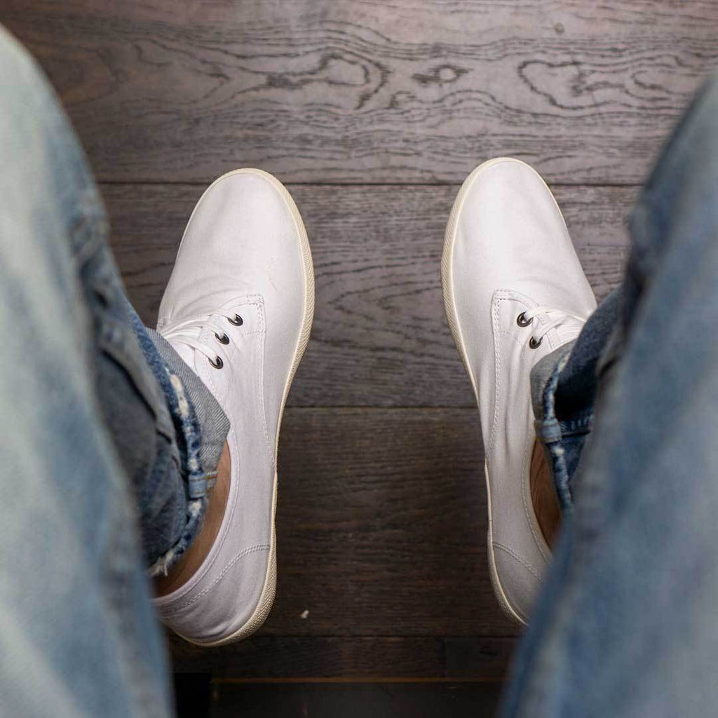 Men's Sixty Six Sneaker in White canvas, viewed from above, worn with jeans on a wood floor