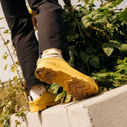Men's Bodega Clog in Calendula rubber, close-up worn with dark pants stepping onto a concrete ledge