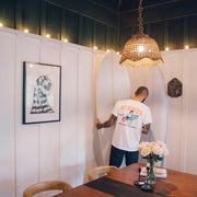 Person in a SeaVees white t-shirt standing beside a surfboard in a dining room