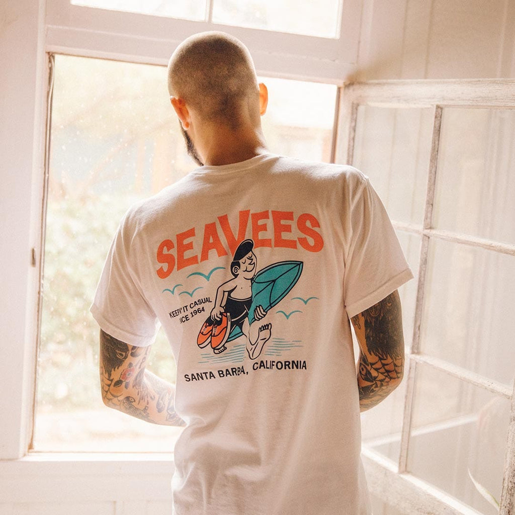 Person in a SeaVees white t-shirt with surfer graphic on the back, facing a window