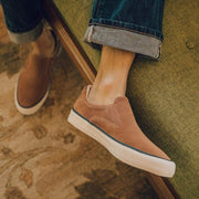 Men's Hawthorne Slip On in Terracotta suede, close-up worn with cuffed jeans on a green sofa