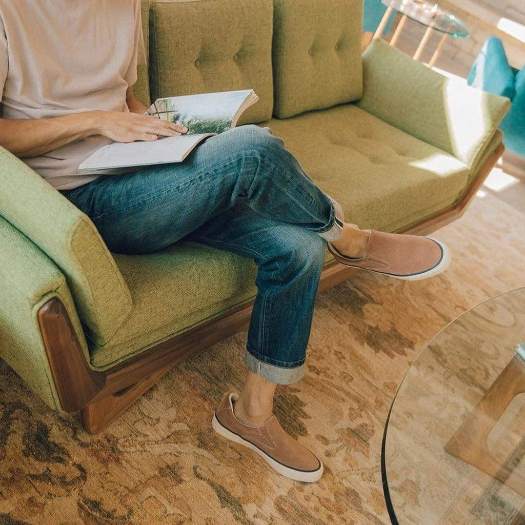 Men's Hawthorne Slip On in Terracotta suede, worn with jeans by a person seated reading on a green sofa