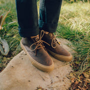 Men's Maslon Desert Boot in Kona leather, worn with cuffed jeans on a stone step