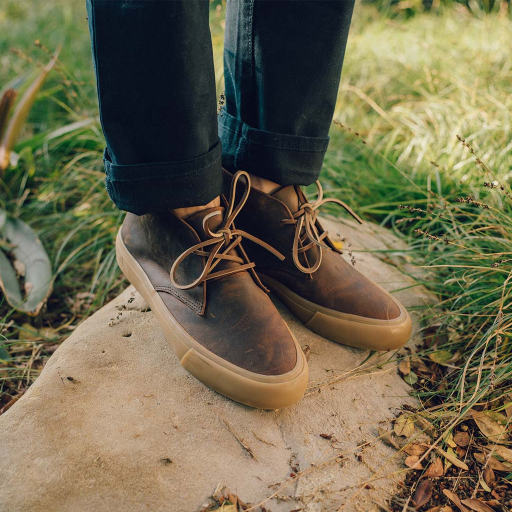 Men's Maslon Desert Boot in Kona leather, worn with cuffed jeans on a stone step