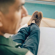 Men's Maslon Desert Boot in Kona leather, worn by a person seated beside a pool with feet crossed