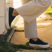 Women's Baja Slip On in True Navy canvas, worn with cream pants, one foot raised outdoors
