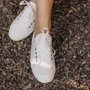 Women's Monterey Sneaker in Bleach canvas, worn with bare ankles on dark mulch, close up
