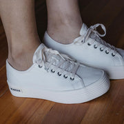Women's Monterey Sneaker in Bleach canvas, worn with bare ankles on a wood floor, side view