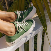 Women's Monterey Sneaker in Cactus canvas, worn with feet resting on a white railing, close up
