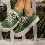 Women's Monterey Sneaker in Cactus canvas, worn with feet raised on a white railing
