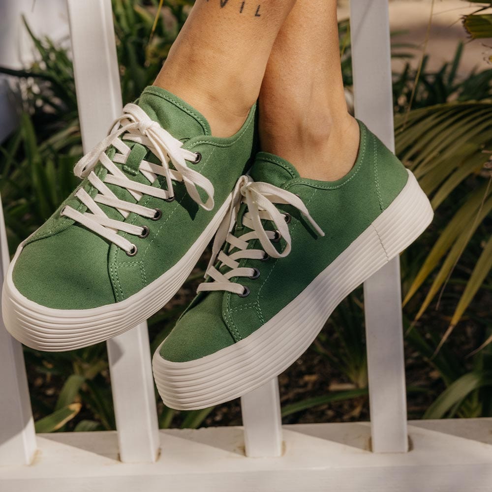 Women's Monterey Sneaker in Cactus canvas, worn with feet raised on a white railing