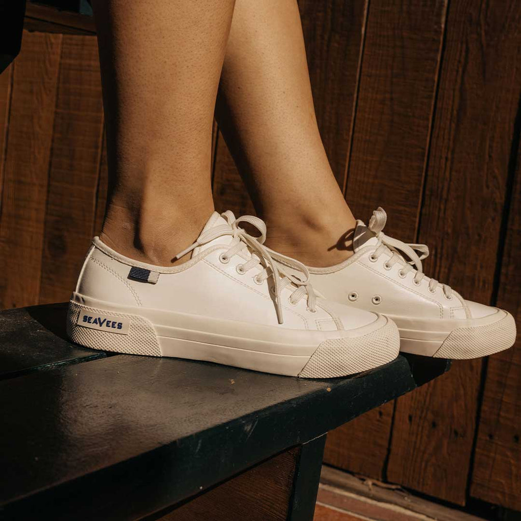 Women's SeaChange LTT sneaker in White Corn Leather, close-up worn on a dark wood bench
