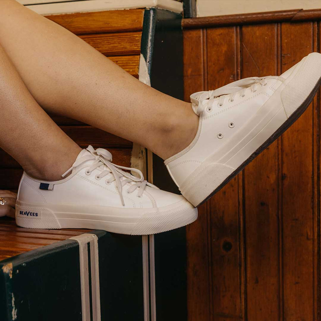 Women's SeaChange LTT sneaker in White Corn Leather, close-up worn with bare ankles on a wood bench