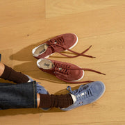 Women's Clipper Sneaker in Cornflower Blue suede, pair of laced shoes beside a second pair in burgundy on a wood floor