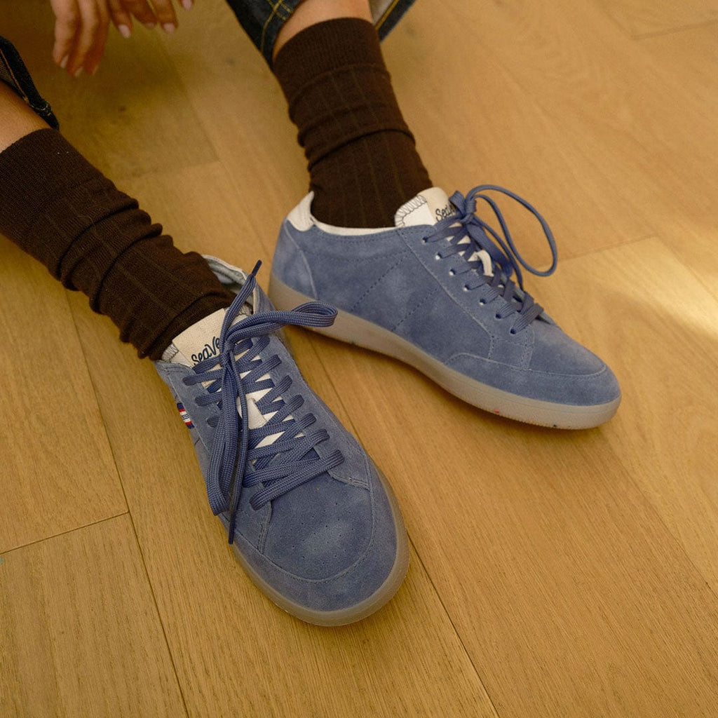 Women's Clipper Sneaker in Cornflower Blue suede, worn with brown socks on a wood floor, close up